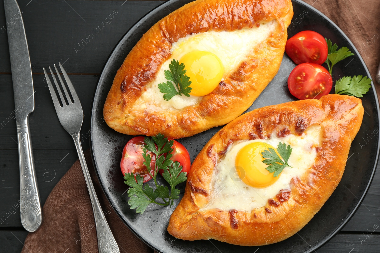 Photo of Tasty khachapuri with cheese and eggs served on black wooden table, flat lay
