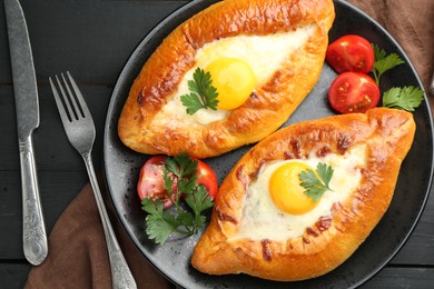Photo of Tasty khachapuri with cheese and eggs served on black wooden table, flat lay