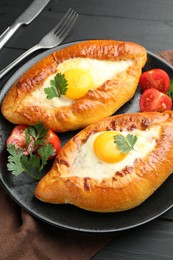 Photo of Tasty khachapuri with cheese and eggs served on black wooden table, closeup