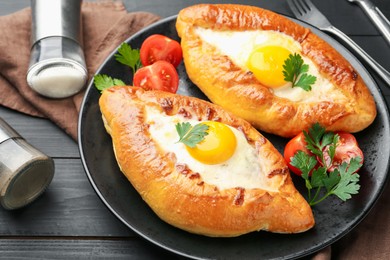 Photo of Tasty khachapuri with cheese and eggs served on black wooden table, closeup