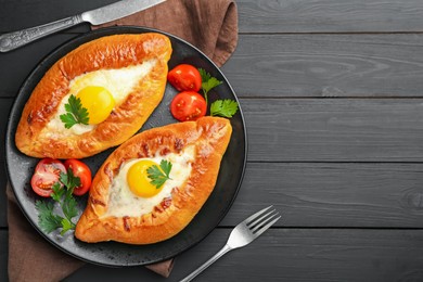 Photo of Tasty khachapuri with cheese and eggs served on black wooden table, flat lay. Space for text