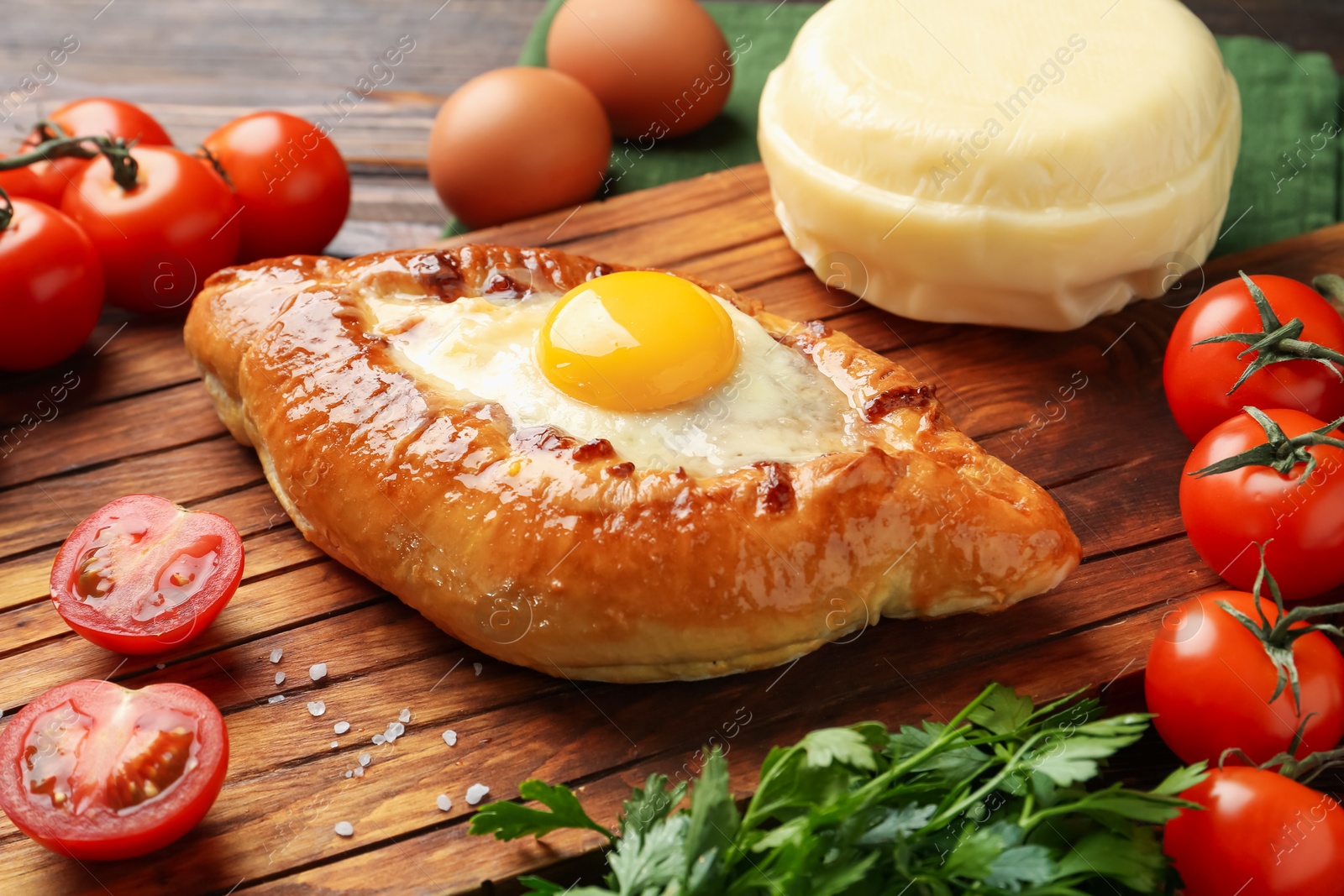 Photo of Tasty khachapuri with cheese, eggs and other products on wooden table, closeup