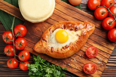 Photo of Tasty khachapuri with cheese, egg and other products on wooden table, flat lay