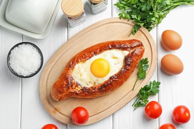 Photo of Tasty khachapuri with cheese, eggs and other products on white wooden table, flat lay