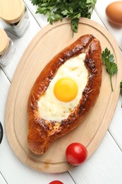 Photo of Tasty khachapuri with cheese, eggs and other products on white wooden table, flat lay