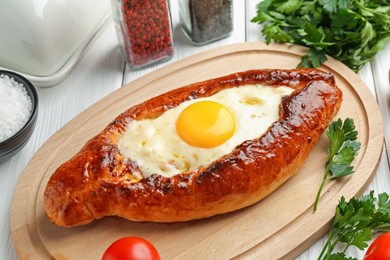 Photo of Tasty khachapuri with cheese, egg and other products on white wooden table, closeup