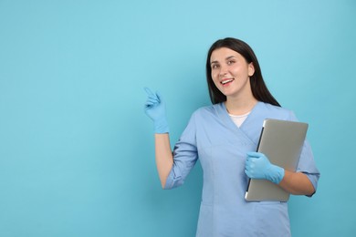 Photo of Nurse with laptop pointing at something on light blue background, space for text