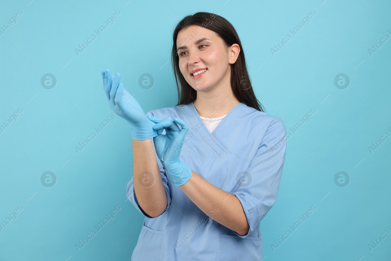 Photo of Nurse in uniform wearing gloves on light blue background