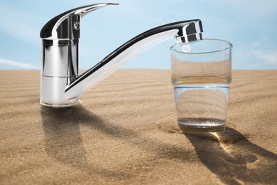 Image of Save water concept. Glass under tap with dripping water in desert