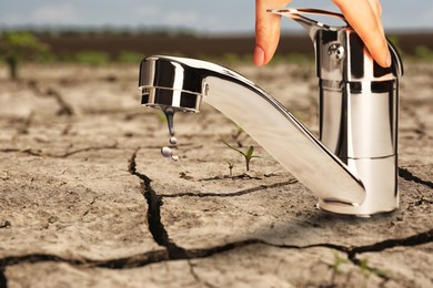 Image of Save water concept. Woman turning on or off tap on cracked ground, closeup