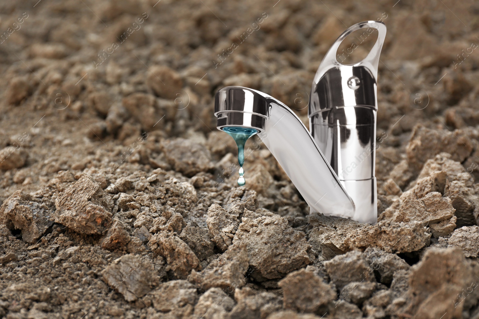 Image of Save water concept. Tap with dripping water in dry ground