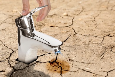 Image of Save water concept. Man turning on or off tap on cracked ground, closeup