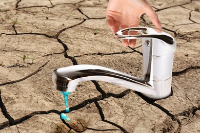 Image of Save water concept. Woman turning on or off tap on cracked ground, closeup