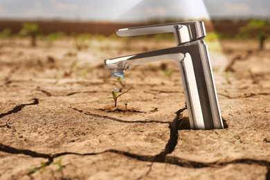 Image of Save water concept. Tap with dripping water in scorched earth