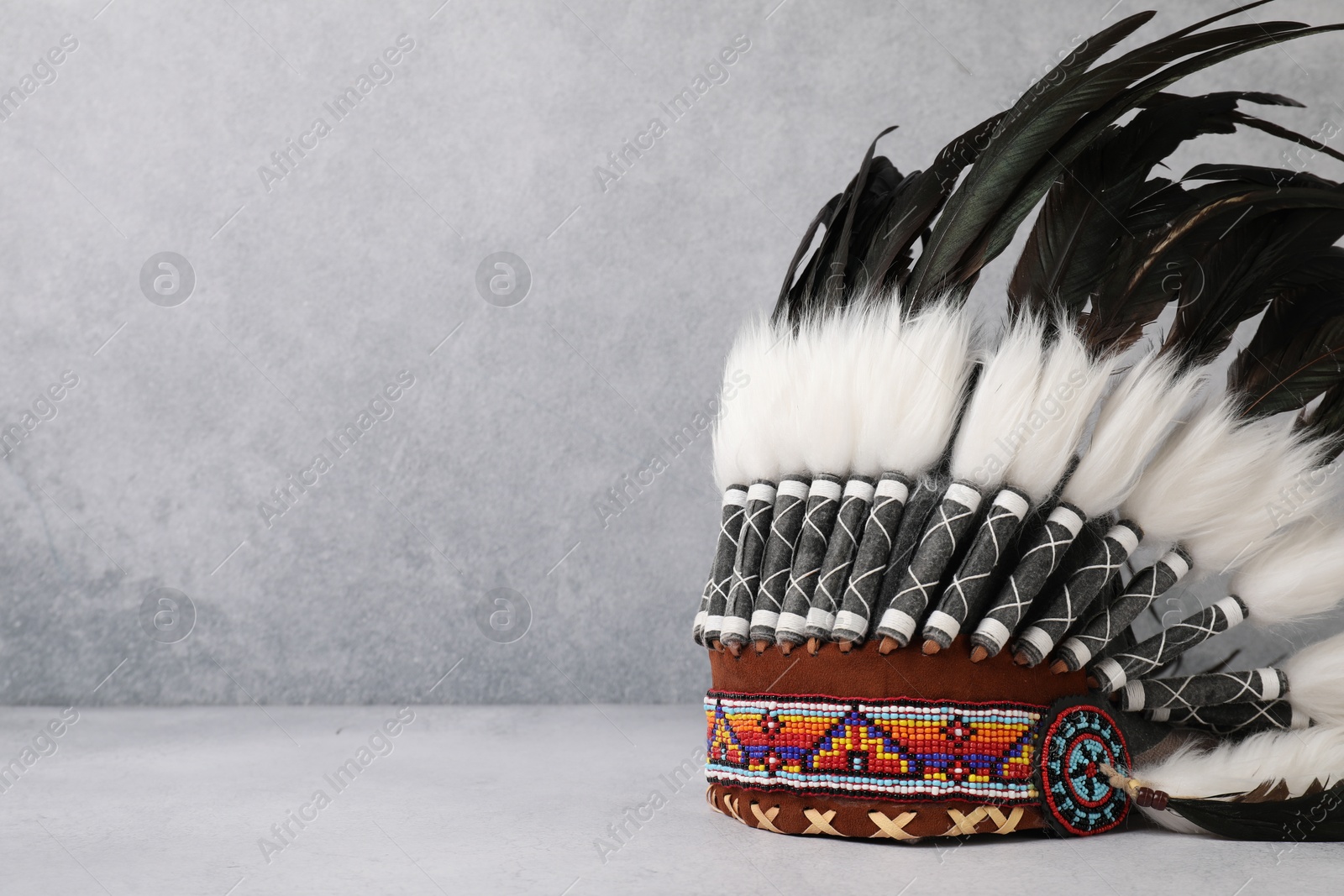 Photo of Traditional warbonnet (Native American chief headdress) on light grey table, space for text