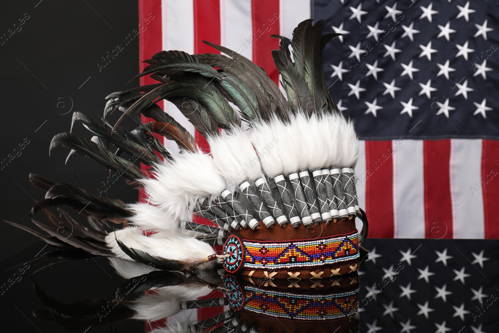 Photo of Traditional warbonnet (Native American chief headdress) on black mirror surface against flag of USA