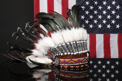 Photo of Traditional warbonnet (Native American chief headdress) on black mirror surface against flag of USA