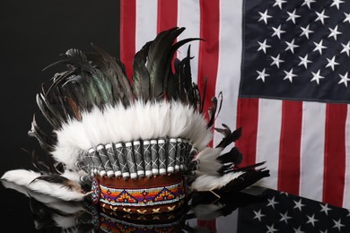 Photo of Traditional warbonnet (Native American chief headdress) on black mirror surface against flag of USA