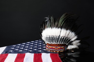 Photo of Traditional warbonnet (Native American chief headdress) and flag of USA on black mirror surface