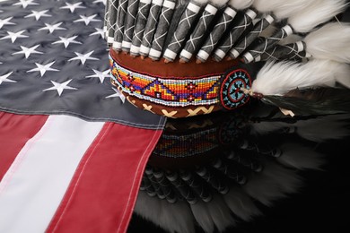 Photo of Traditional warbonnet (Native American chief headdress) and flag of USA on black mirror surface, closeup