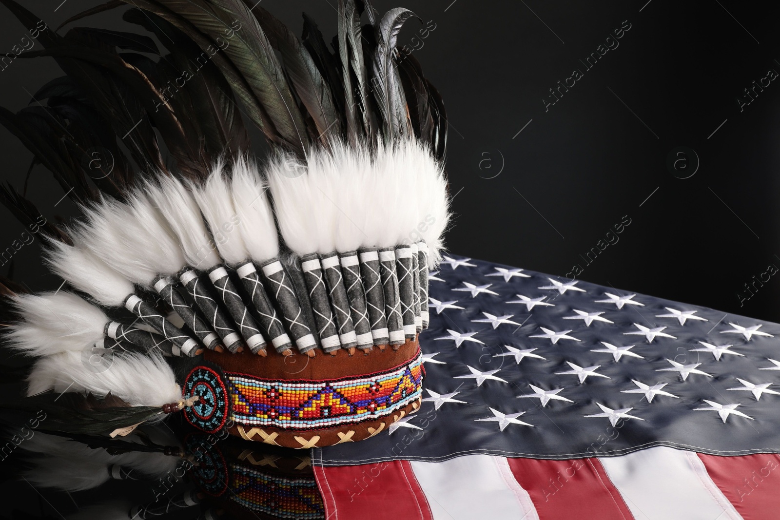 Photo of Traditional warbonnet (Native American chief headdress) and flag of USA on black mirror surface