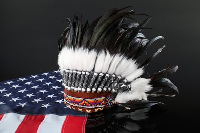 Photo of Traditional warbonnet (Native American chief headdress) and flag of USA on black mirror surface