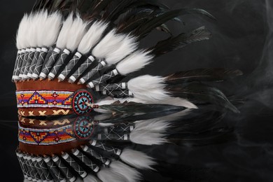 Photo of Traditional warbonnet (Native American chief headdress) in smoke on black mirror surface