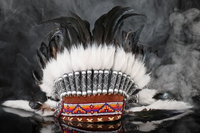 Photo of Traditional warbonnet (Native American chief headdress) in smoke on black mirror surface