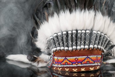 Photo of Traditional warbonnet (Native American chief headdress) in smoke on black mirror surface, closeup