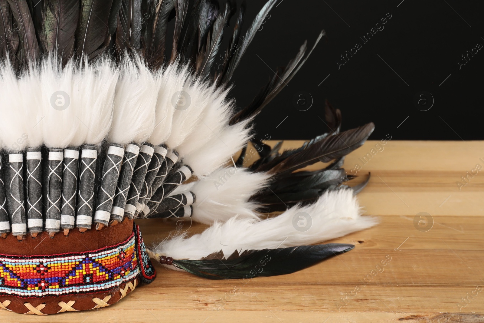 Photo of Traditional warbonnet (Native American chief headdress) on wooden table against black background, closeup