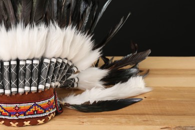 Photo of Traditional warbonnet (Native American chief headdress) on wooden table against black background, closeup