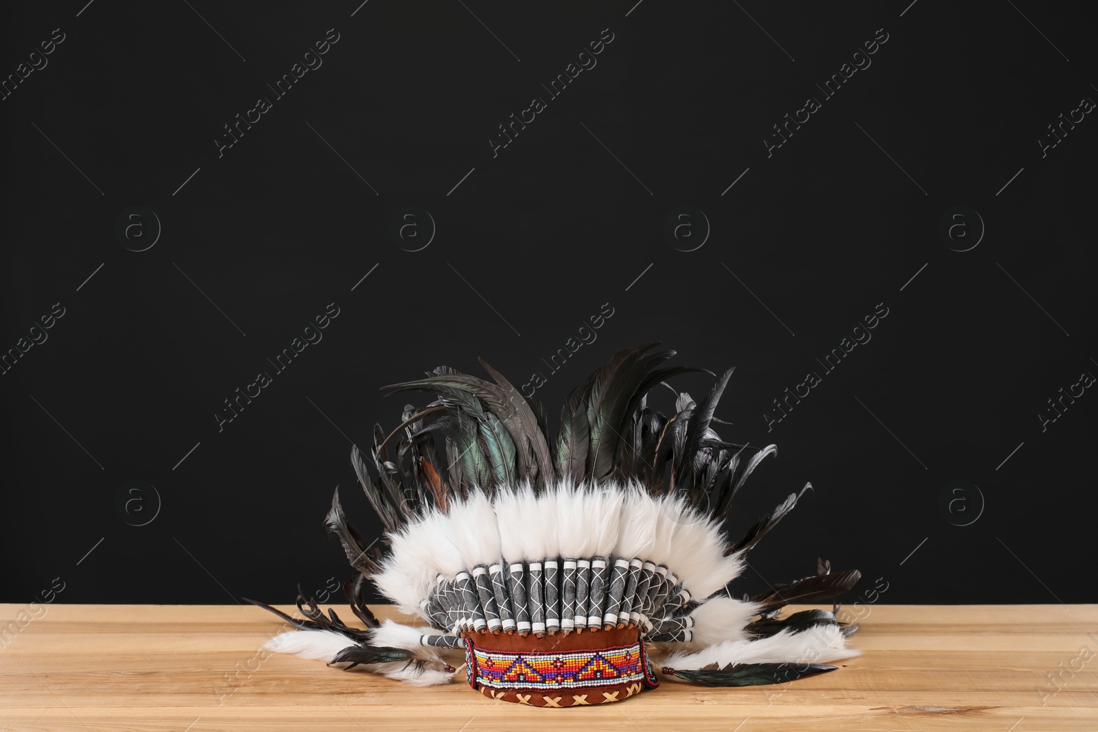 Photo of Traditional warbonnet (Native American chief headdress) on wooden table against black background