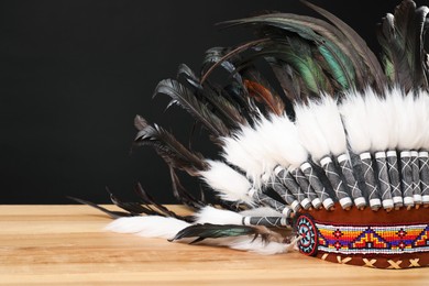 Photo of Traditional warbonnet (Native American chief headdress) on wooden table against black background, closeup