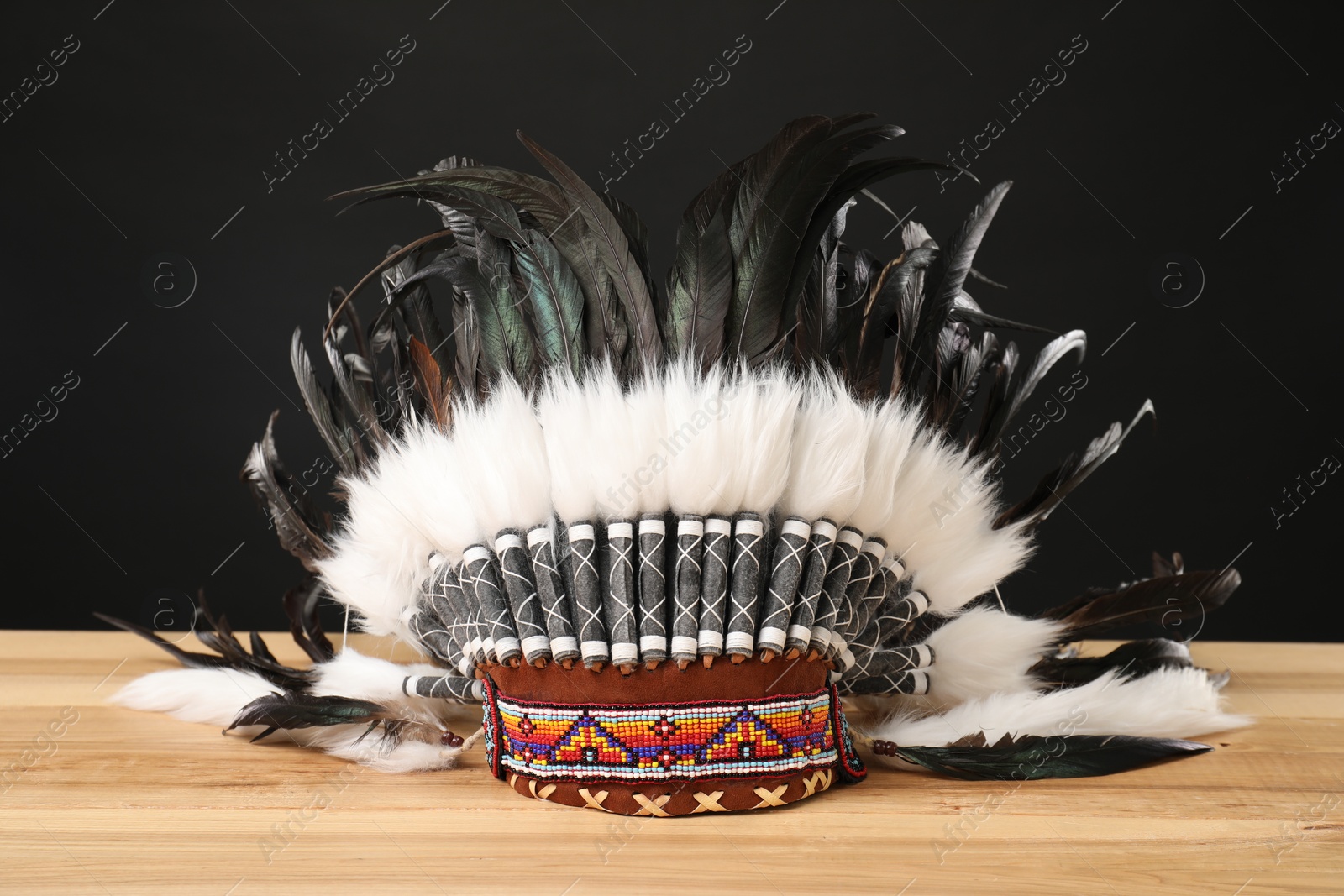 Photo of Traditional warbonnet (Native American chief headdress) on wooden table against black background