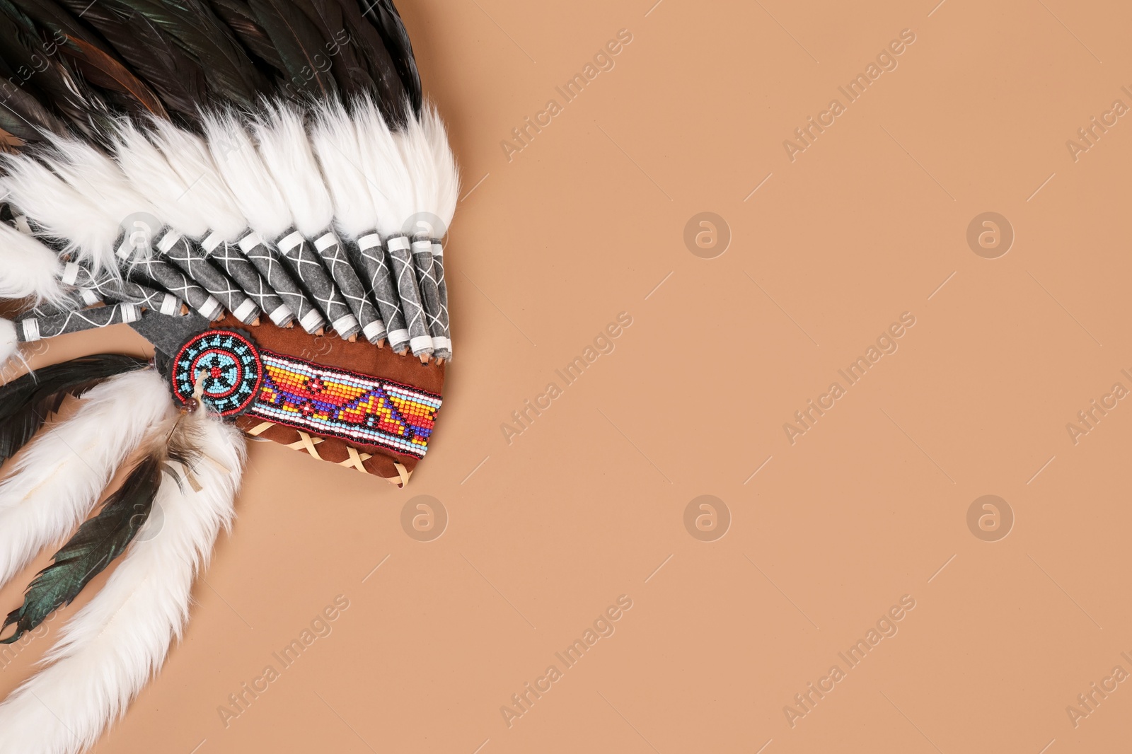 Photo of Traditional warbonnet (Native American chief headdress) on beige background, top view. Space for text