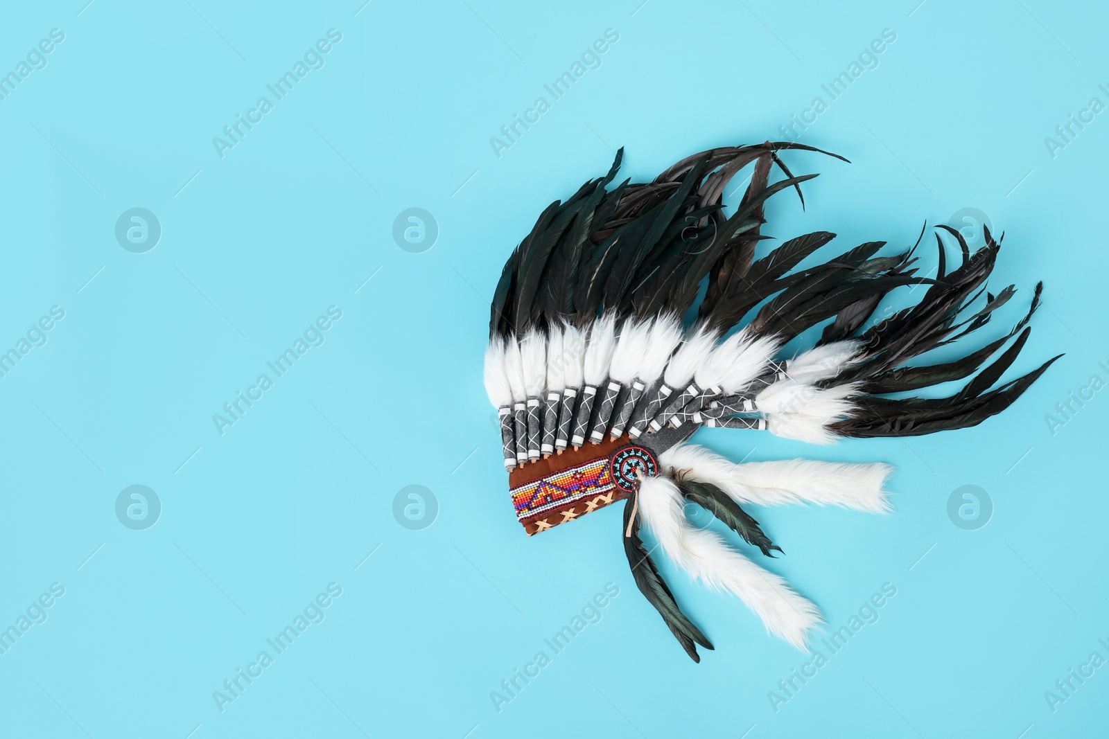 Photo of Traditional warbonnet (Native American chief headdress) on light blue background, top view. Space for text