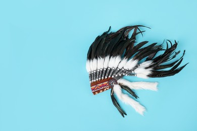 Photo of Traditional warbonnet (Native American chief headdress) on light blue background, top view. Space for text