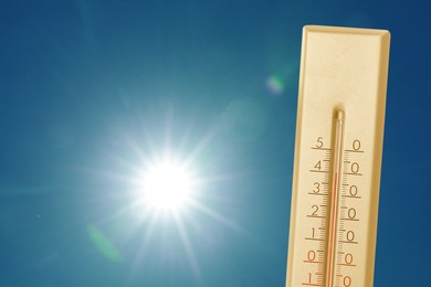 Image of Thermometer showing high temperature against sky with bright sun. Extremely hot weather