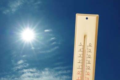 Image of High temperature on thermometer against blue sky with clouds and bright sun. Extremely hot weather