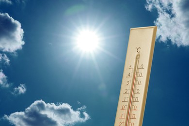 Image of High temperature on thermometer against blue sky with clouds and bright sun. Extremely hot weather
