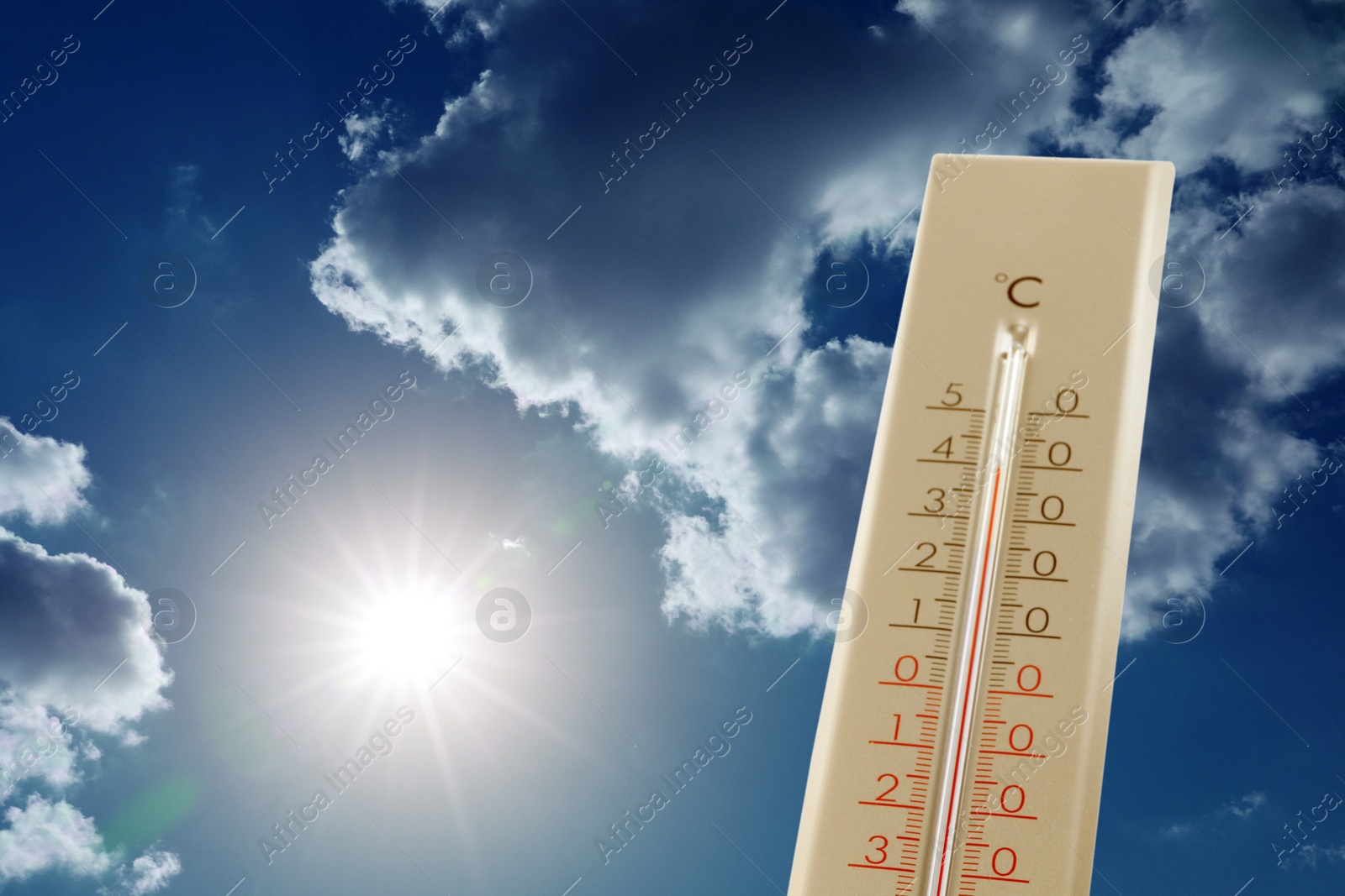 Image of High temperature on thermometer against blue sky with clouds and bright sun. Extremely hot weather