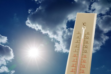 Image of High temperature on thermometer against blue sky with clouds and bright sun. Extremely hot weather