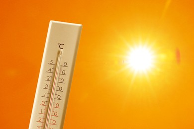 Image of Thermometer showing high temperature against orange sky with bright sun. Extremely hot weather