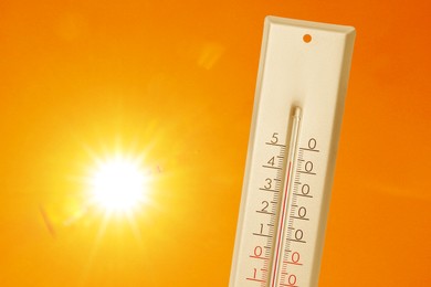 Image of Thermometer showing high temperature against orange sky with bright sun. Extremely hot weather