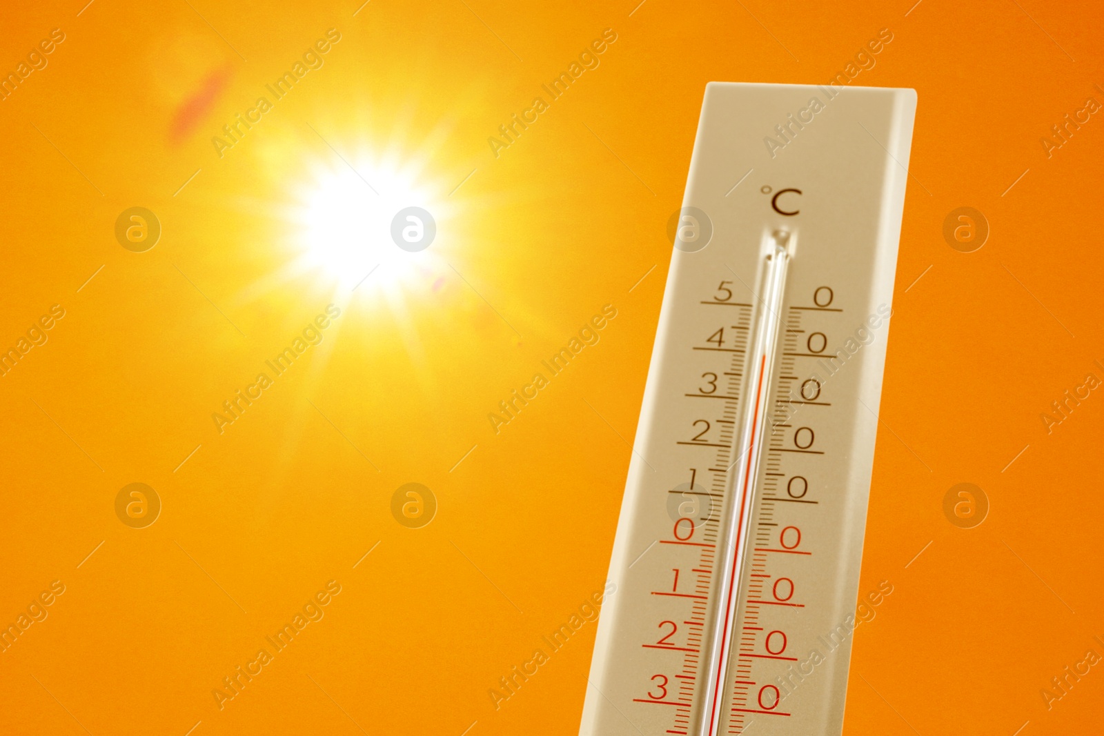 Image of Thermometer showing high temperature against orange sky with bright sun. Extremely hot weather