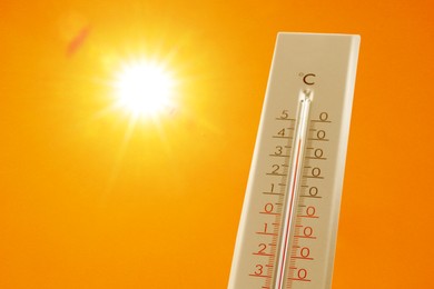 Image of Thermometer showing high temperature against orange sky with bright sun. Extremely hot weather