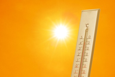 Image of Thermometer showing high temperature against orange sky with bright sun. Extremely hot weather