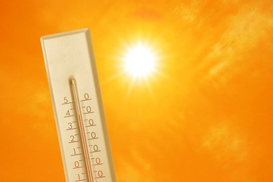 Image of Thermometer showing high temperature against orange sky with bright sun. Extremely hot weather
