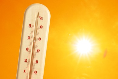 Image of Thermometer showing high temperature against orange sky with bright sun. Extremely hot weather