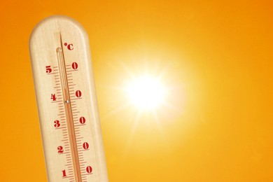 Image of Thermometer showing high temperature against orange sky with bright sun. Extremely hot weather